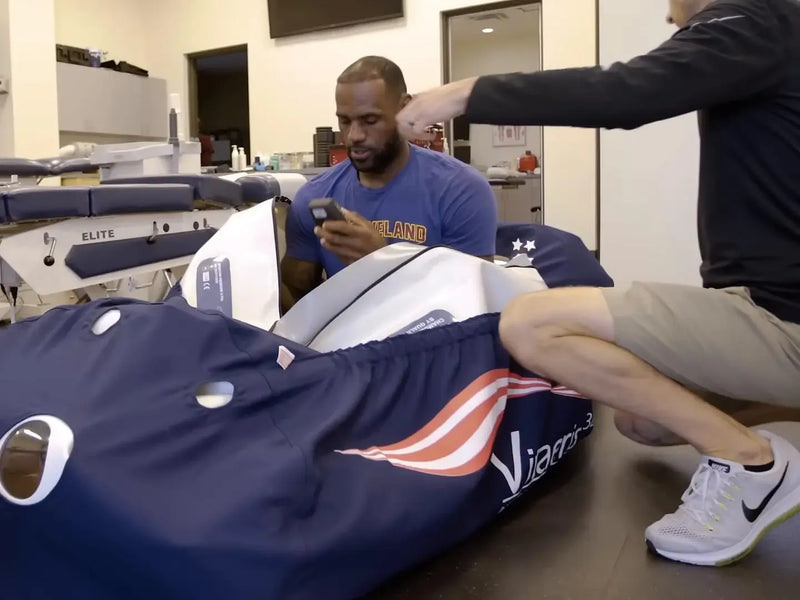 LeBron James sits inside an open OxyHealth Vitaeris 320® chamber in a team training room.